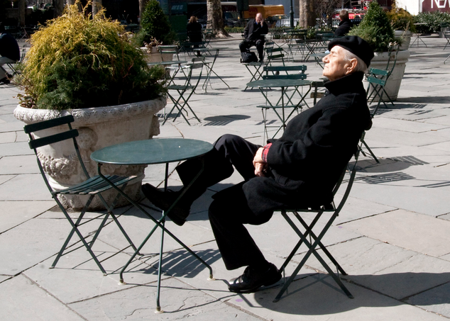 an older man reclining in a small green chair in a public park